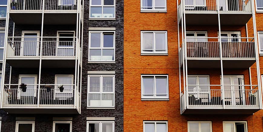 Four floors of two blocks of flats joined together, one red brick, one black bricks, both have balconies, 8 in total are visible