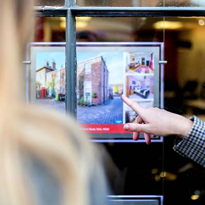 Two people, one pointing, looking a house for sale in estate agents window