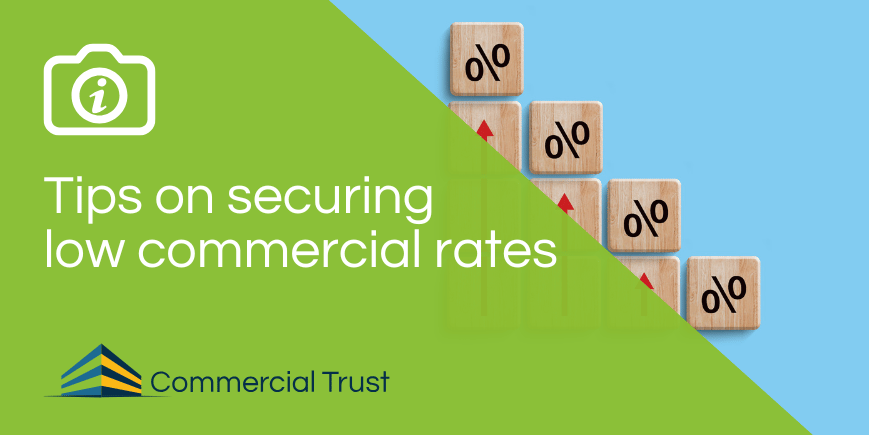 Green banner with text "Tips on securing low commercial rates" overlaid on a picture of wooden tiles with the interest rate symbol on them