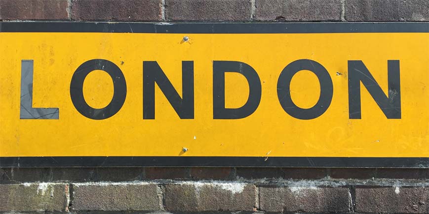 Yellow 'London' road sign, with black lettering on brick wall