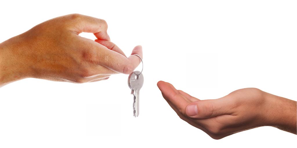 Two hands against a white background, one handing a door key to the other