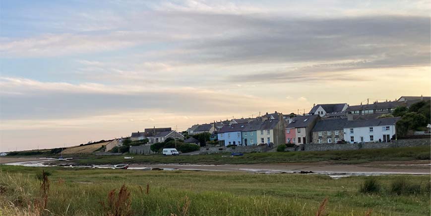 Coastal houses in bright colours and in stone, facing over an inlet from the sea and marshland
