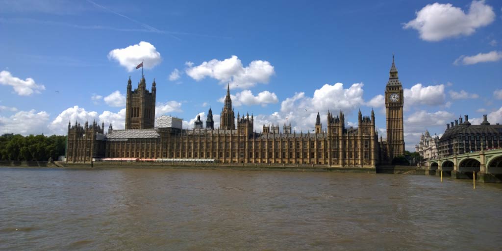 Houses of Parliament on bright sunny day with clouds in the sky and Thames river in foreground
