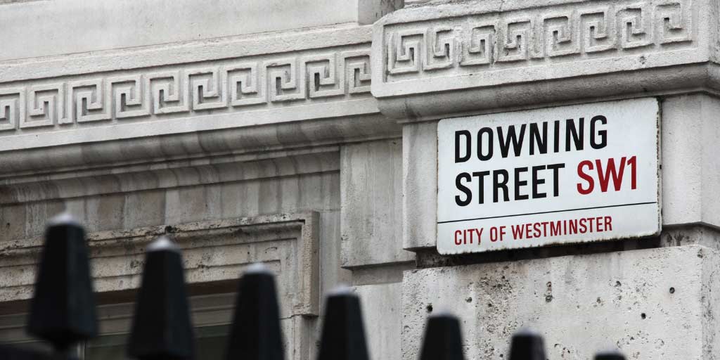 Downing Street SW1 sign on decorative white stone wall with black railings just visible in foreground