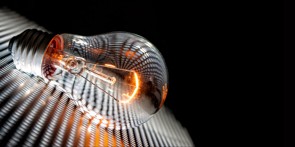 Lit up bulb, sitting on a metal grill, with a black background