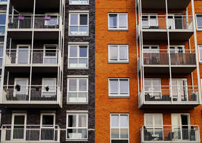 Four floors of two blocks of flats joined together, one red brick, one black bricks, both have balconies, 8 in total are visible